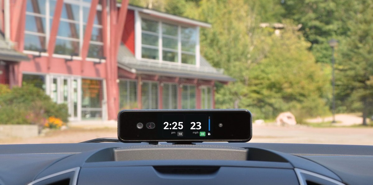 Dashcam mounted on a windshield with its display showing the time and current speed against the road ahead